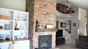 A living room with a brick fireplace, white shelves with decorative items, a television, and a ceiling fan. - Watts Bar Lake House (Spring City)