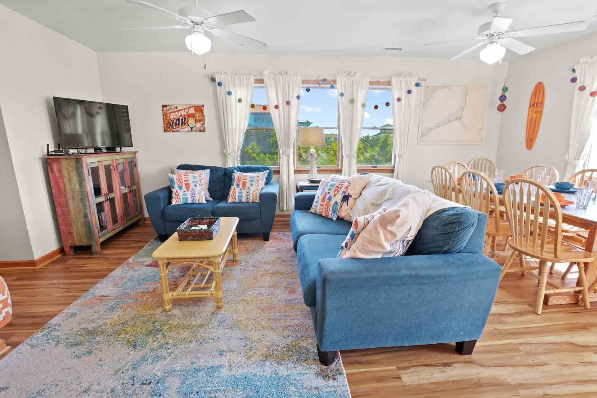A living room with a blue sofa, a wooden coffee table, a TV on a cabinet, and a dining area with wooden chairs and a table.