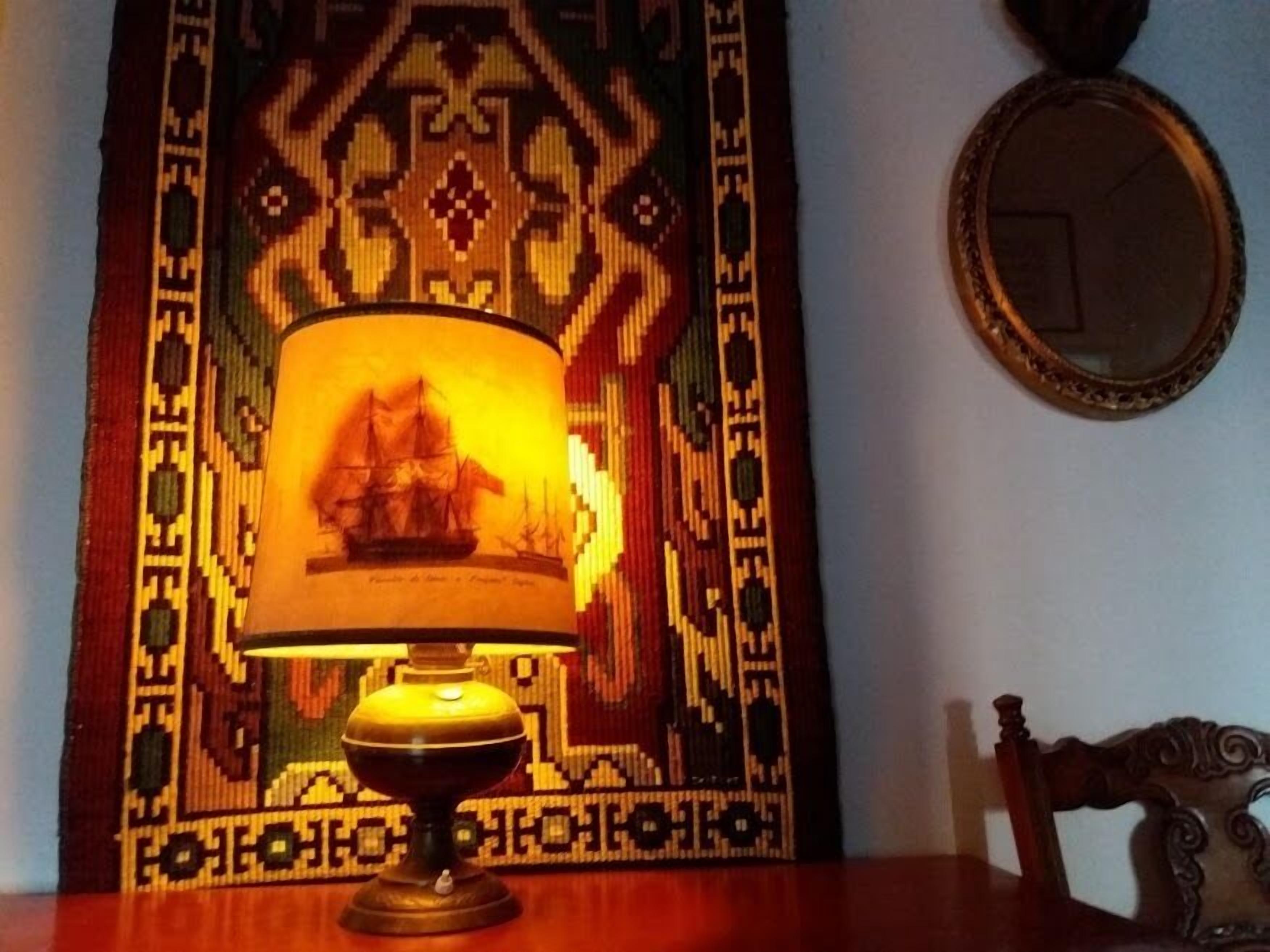A table with a patterned tablecloth, a lamp with a ship design, and a mirror on the wall.