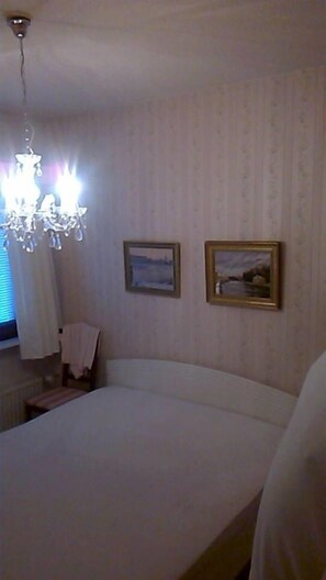 A hotel room with a large bed, a chandelier, two framed pictures on the wall, and a chair. - Spacious 4 Room Apartment & Sauna (Kotka)