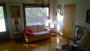 Uma sala de estar com sofá, poltrona, luminária e janela com vista para árvores.