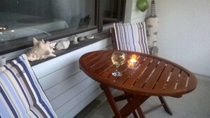 Uma mesa de madeira com um copo de vinho e uma vela acesa, uma cadeira listrada e uma concha decorativa em um peitoril.