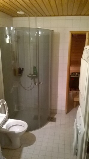 A bathroom with a glass-enclosed shower, a toilet, and a wooden cabinet. - Spacious 4 Room Apartment & Sauna (Kotka)