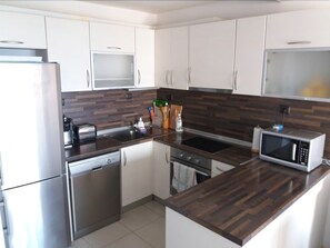 A modern kitchen with white cabinets, stainless steel appliances, and a dark wood countertop. - Varna Seaview Residence (Varna)