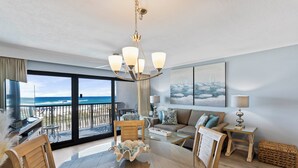 A spacious living room with a large glass door leading to a balcony, a round dining table, and a chandelier. - 214- Adventure to WHITE SANDS and sparkling waters! Destin Beach Club (Destin)