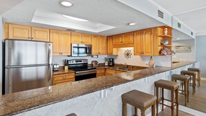 A modern kitchen with wooden cabinets, stainless steel appliances, granite countertops, and bar stools. - 214- Adventure to WHITE SANDS and sparkling waters! Destin Beach Club (Destin)