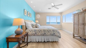Un dormitorio con una cama grande, un ventilador de techo y vistas al océano a través de amplios ventanales.