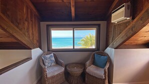 A cozy corner with two wicker chairs, a small round table, and a window offering a view of the ocean.