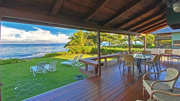 A covered outdoor area with a wooden deck, lounge chairs, and a table set for dining.