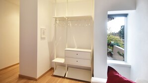 Una habitación con un armario blanco, una mesita y una ventana con vistas a la vegetación.