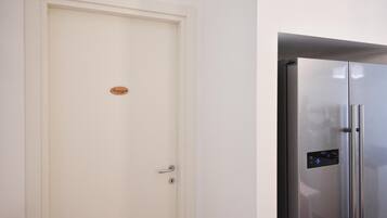 Une porte blanche fermée, ornée d’une petite plaque, et un réfrigérateur moderne en acier inoxydable doté d’un panneau de commande numérique.