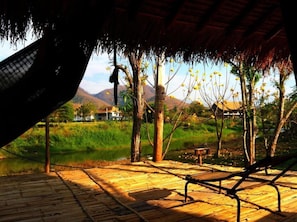 A wooden deck with a hammock, a bench, and a thatched roof structure. - Giant House Riverside (Pai)