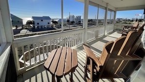 Eine überdachte Veranda mit Holzmöbeln und Blick auf Strand und Gebäude.