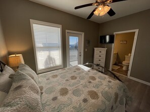 A bedroom with a bed, a ceiling fan, a dresser, and a view of the outside.