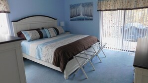 Une chambre à coucher avec un lit, une table de chevet, un ventilateur de plafond et une fenêtre avec des rideaux.