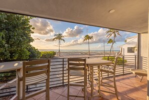 A covered outdoor seating area with a view of the beach and palm trees. - Enjoy brilliant sunsets over the sapphire waters (Captiva)