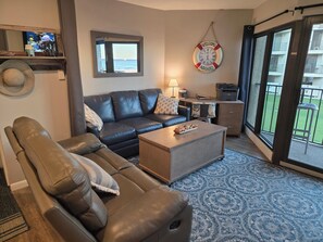A living room with a sofa, a coffee table, a lamp, and a view of the ocean through a window.