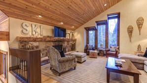 Un salon chaleureux avec une cheminée en pierre, un plafond en bois et une grande fenêtre.