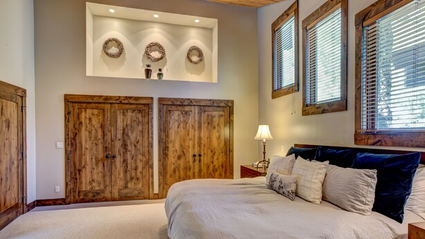 Un dormitorio con una cama grande, un armario de madera y un estante en la pared con objetos decorativos.