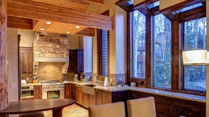 Una cocina rústica con chimenea de piedra, armarios de madera y un ventanal con vistas a un bosque.