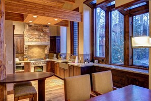 Eine rustikale Küche mit Kamin aus Stein, Holzschränken und einem großen Fenster mit Blick auf einen Wald.