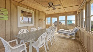 A wooden deck with a table and chairs, a ceiling fan, and large windows overlooking the beach. - Semi-Oceanfront Dog Friendly Avon Home w/ Private Pool, Hot Tub, and Game Room (Avon)