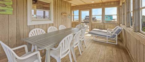 A wooden deck with a table and chairs, a ceiling fan, and large windows overlooking the beach.