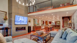 A spacious living room with a large flat-screen TV, a fireplace, and a dining area in the background. - Luxury in Central Location. Shuttle outside door! Pool Table, Hot Tub, Ultra Lux (Park City)