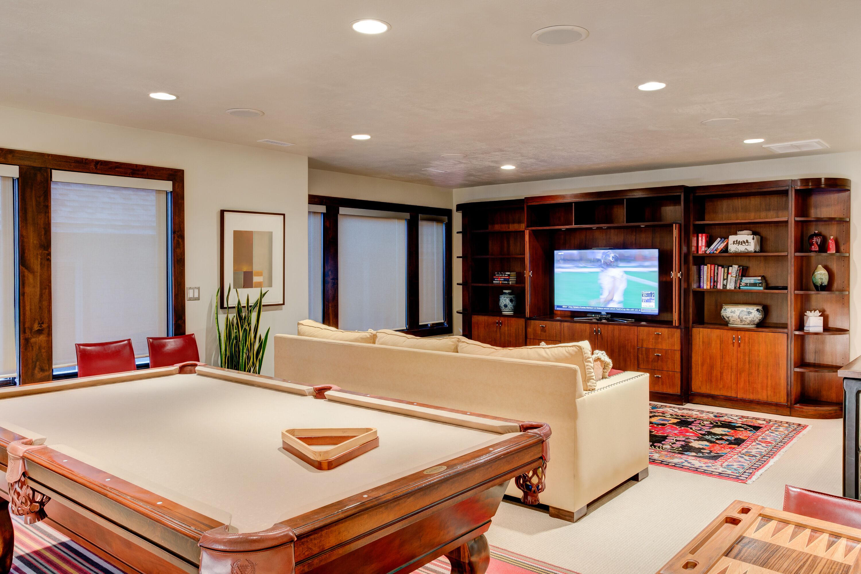 Un salon comprenant une table de billard, un canapé, un téléviseur et des meubles de rangement en bois.