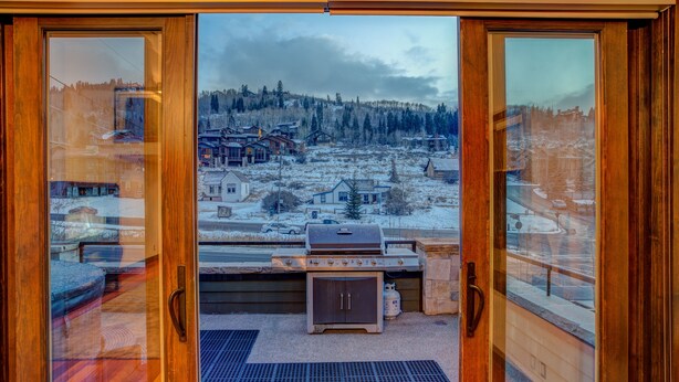 A wooden-framed glass door leading to an outdoor patio with a grill and a view of a snowy village. - Luxury in Central Location. Shuttle outside door! Pool Table, Hot Tub, Ultra Lux (Park City)