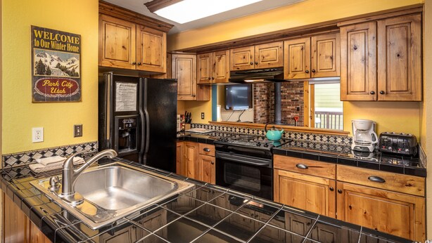 A kitchen with wooden cabinets, a stainless steel sink, a refrigerator, a stove, and a coffee maker. - Heart of PC! 2 blocks from lift! Shuttle to Main in 3 minutes! Cozy w/ hot tub! (Park City)