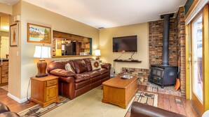 A cozy living room with a brown leather sofa, wooden side tables, a flat-screen TV, and a fireplace. - Heart of PC! 2 blocks from lift! Shuttle to Main in 3 minutes! Cozy w/ hot tub! (Park City)