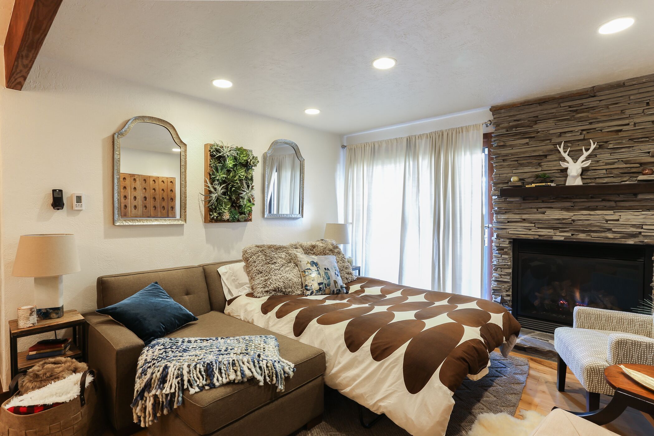 A bedroom with a large bed, a sofa, a fireplace, and a stone wall.