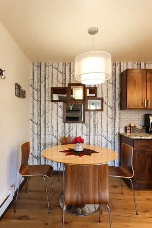 A dining area with a round table, four chairs, a chandelier, and a wall with a tree pattern. - POW HAUS: Modern Beaver Creek 2BR w/ Ski Access (Avon)