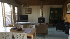 Una sala de estar acogedora con una mesa de madera, sillas, un sofá, un televisor y una chimenea.