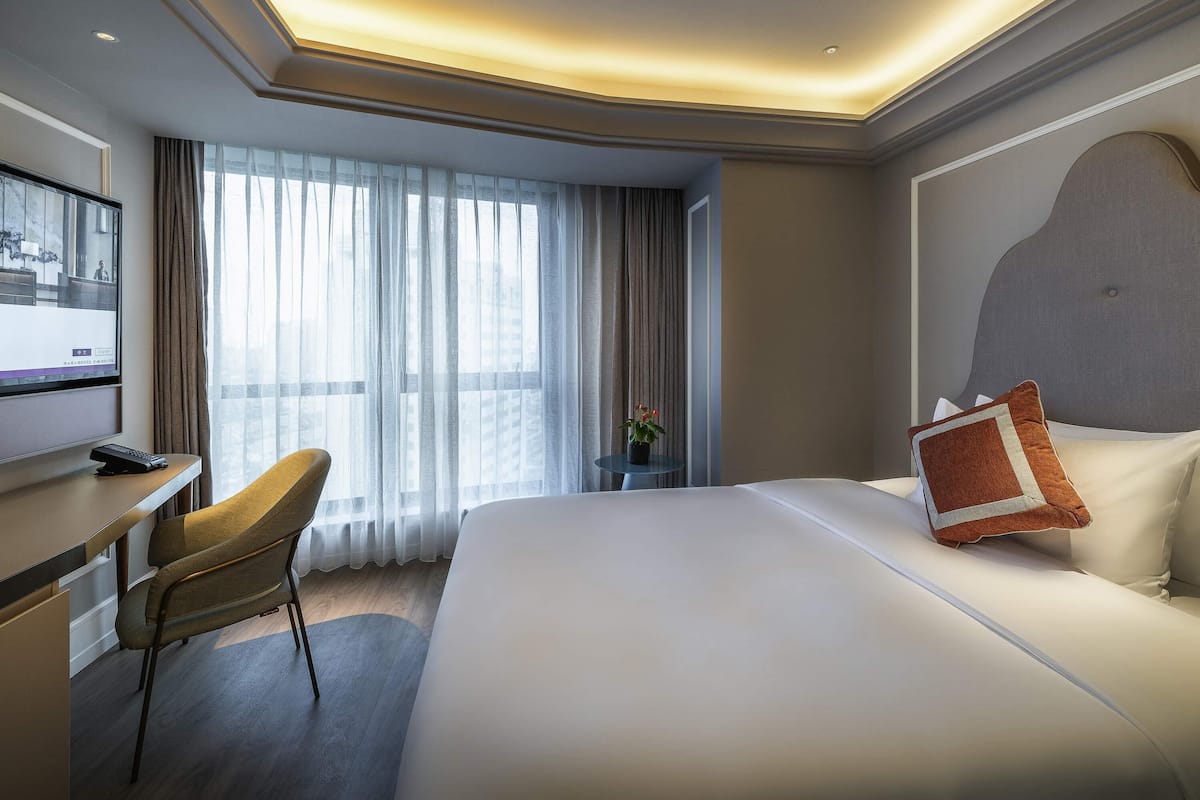 Ein Hotelzimmer mit Bett, Schreibtisch, Stuhl, Fernseher und einem fenster mit Vorhängen.