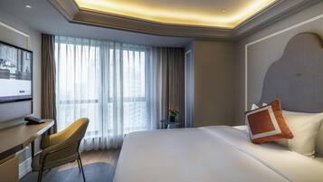 A hotel room with a bed, a desk, a chair, a TV, and a window with curtains.