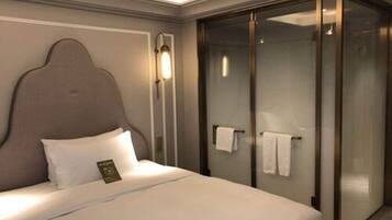 A hotel room with a bed, a headboard, a glass shower enclosure, and a towel rack.