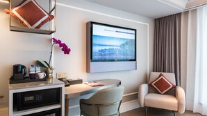 Une chambre d’hôtel moderne équipée d’un bureau, d’un fauteuil confortable, d’une horloge numérique, d’une machine à café et d’une grande fenêtre avec des rideaux.