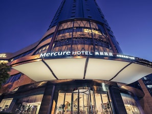 El exterior del Hotel Mercure, con un diseño arquitectónico moderno, destaca por una entrada imponente y señalización iluminada.