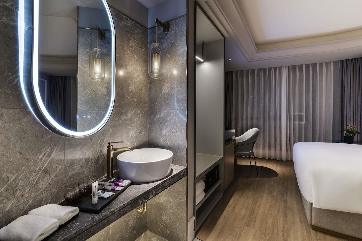 Une salle de bain moderne avec un miroir rond, un lavabo blanc et une commode où sont rangées des serviettes et des articles de toilette.