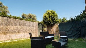 An outdoor seating area with wicker furniture and a glass table, surrounded by a bamboo fence and greenery.