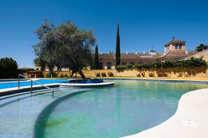A swimming pool with a fountain, surrounded by a landscaped area with trees and a building in the background.