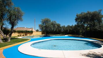 Una piscina circular con borde azul, rodeada de árboles y un edificio al fondo.