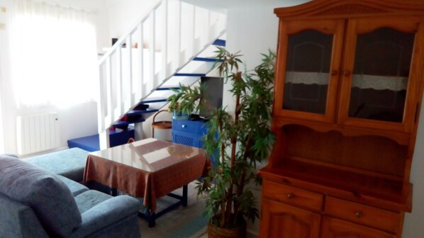 A living room with a staircase, a sofa, a wooden cabinet, and a potted plant.