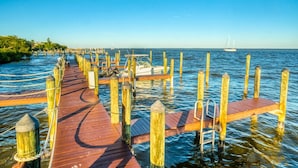 A wooden pier extending into calm waters with a sailboat in the distance.