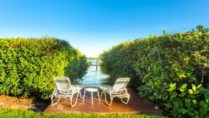 A pathway leading to a water body with two lounge chairs and a small table.