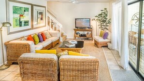 A living room with wicker furniture, a television, and a staircase.