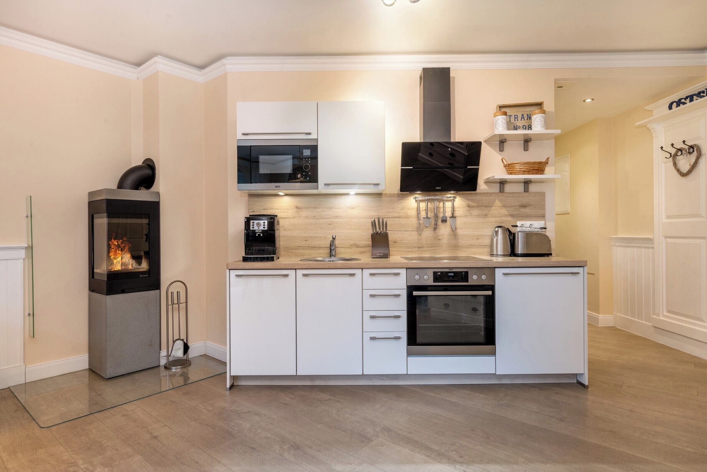 Een moderne keuken met witte kasten, een ingebouwde magnetron, een fornuis en een koffiezetapparaat.