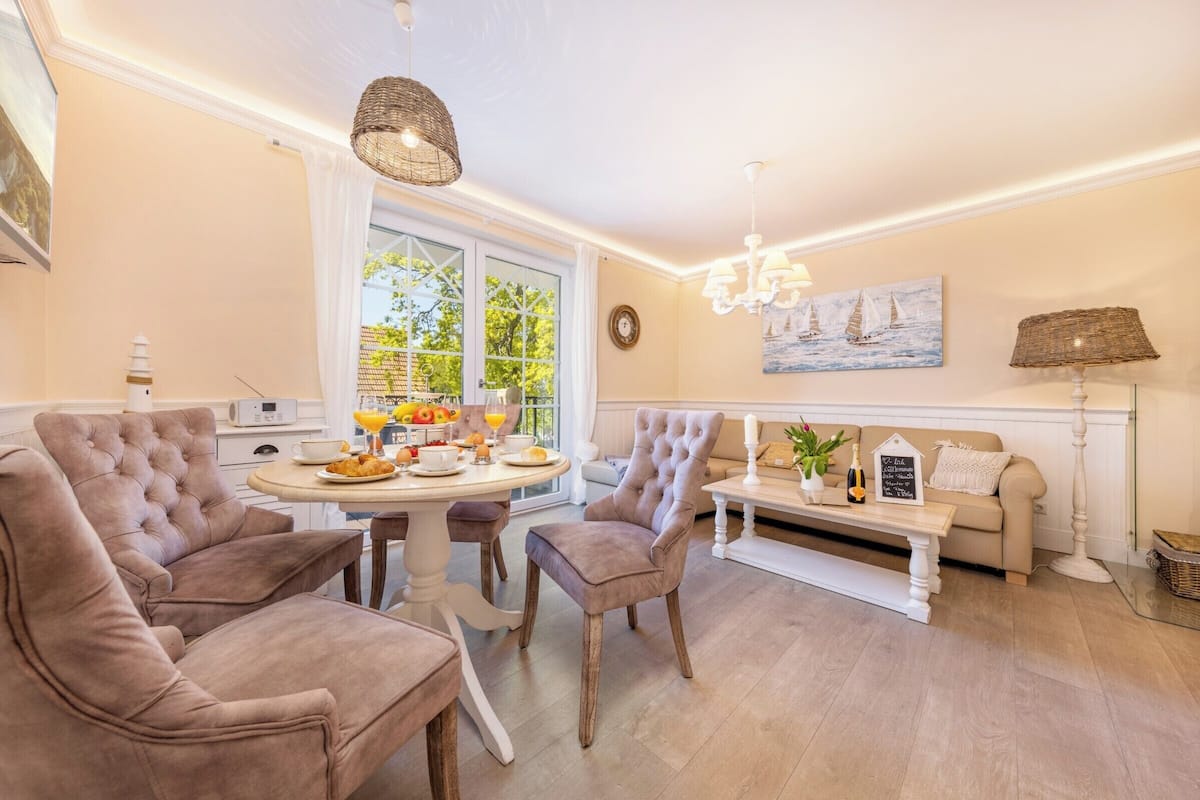 A dining area with a round table, cushioned chairs, and a chandelier.